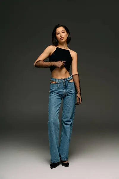 A chic young woman stands tall in relaxed jeans and a stylish top, showcasing her fashion sense. — Stock Photo