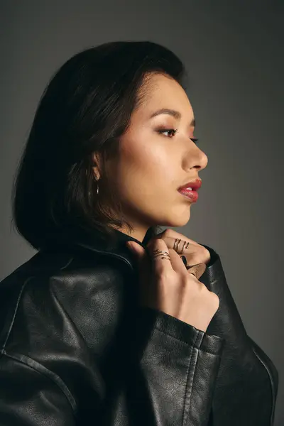 Una joven mujer respira confianza en una chaqueta de cuero chic, golpeando una pose potente y elegante. - foto de stock