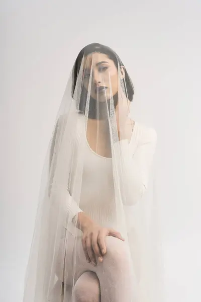 A young bride sits gracefully, her veil gently framing her face with elegance and beauty. — Stock Photo