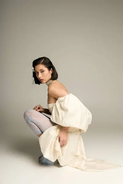 Beautiful young bride squats elegantly, wearing a flowing white gown and a charming expression. — Stock Photo