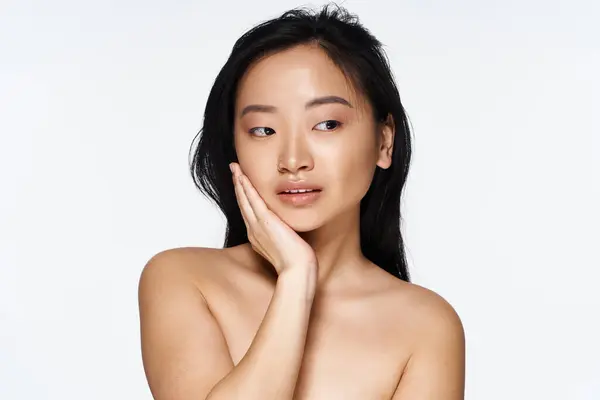 Young asian woman expresses elegance while softly touching her face, exuding confidence and beauty. — Stock Photo