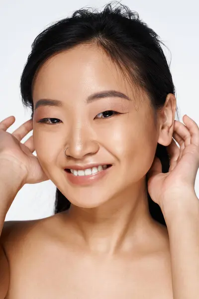 A cheerful young Asian woman smiles while playfully fixing her hair, exuding confidence. — Stock Photo