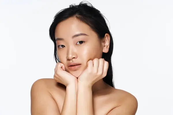 A young Asian woman poses confidently, framing her face in a minimalist setting. — Stock Photo