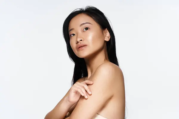 A young asian woman strikes a graceful pose against a simple backdrop, radiating beauty and poise. — Stock Photo