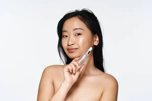 A young Asian woman exudes confidence and grace while holding a skincare serum. — Stock Photo