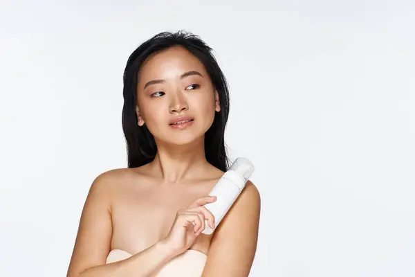 A young asian woman radiates confidence while holding a skincare product, embracing her beauty. — Stock Photo
