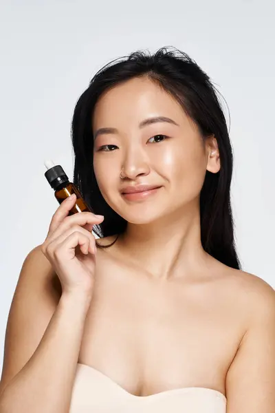 A young asian woman confidently displays a beauty product while radiating charm and confidence. — Stock Photo
