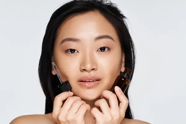 A young woman confidently displays skincare products, her radiant skin glowing in soft light. — Stock Photo