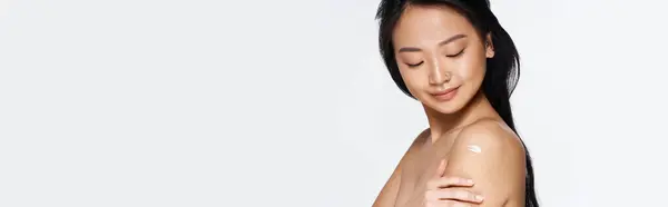 Beautiful young asian woman gently touches her arm, highlighting smooth skin in soft lighting — Stock Photo