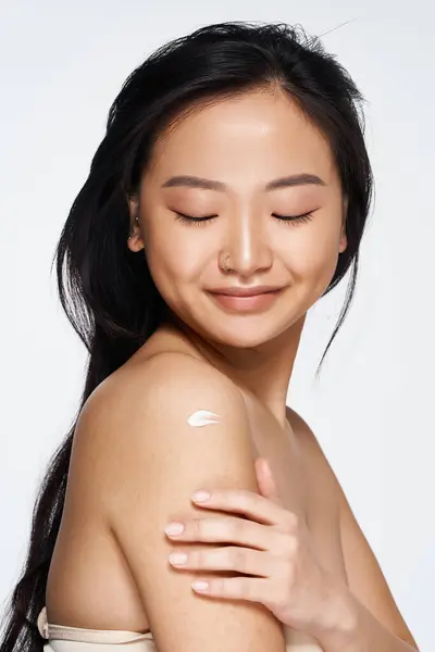 A young Asian woman enjoys a moment of self care, applying lotion with a gentle smile. — Stock Photo