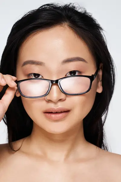 A young Asian woman adjusts her glasses while expressing confidence and charisma in a close up. — Stock Photo