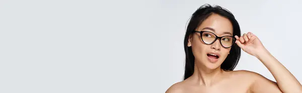 A young woman playfully adjusts her glasses, exuding confidence in a chic backdrop. — Stock Photo