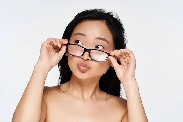 Eine junge Asiatin justiert spielerisch ihre Brille mit nachdenklichem Gesichtsausdruck, während sie posiert. — Stockfoto