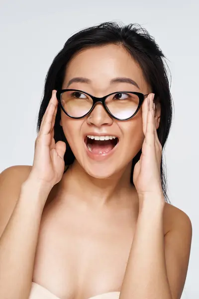 A young asian woman shows her excitement with a big smile, highlighting her stylish glasses. — Stock Photo