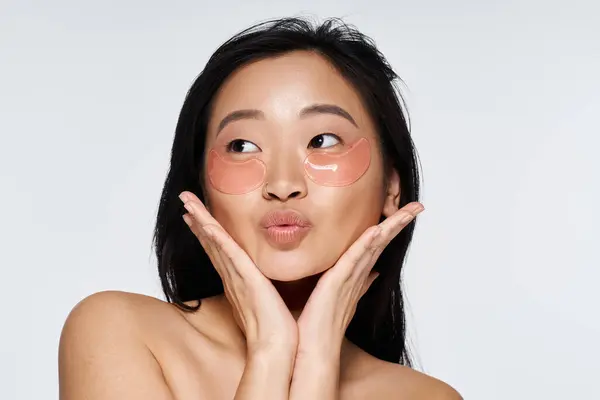 A young Asian woman applies soothing patches, showcasing her radiant beauty and happiness. — Stock Photo