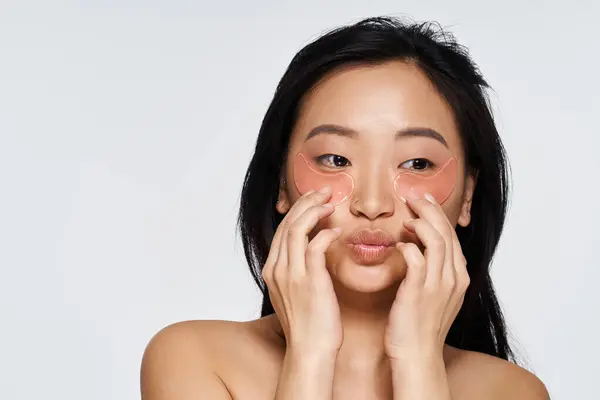 A young asian woman smiles while using hydration patches on her face, engaging in self care. — Stock Photo