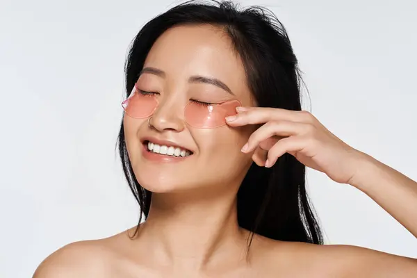 A young woman is smiling joyfully while applying beauty patches with delight and confidence. — Stock Photo