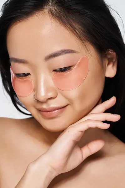 A beautiful young woman applies under eye patches to rejuvenate her skin while smiling softly. — Stock Photo