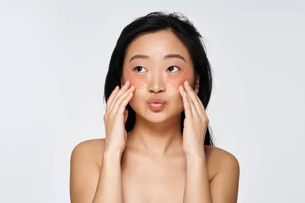 A young asian woman applies hydrating eye patches while engaging in her morning skincare ritual. — Stock Photo