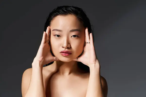 Young asian woman poses with hands on her face, showcasing a thoughtful expression and elegance. — Stock Photo