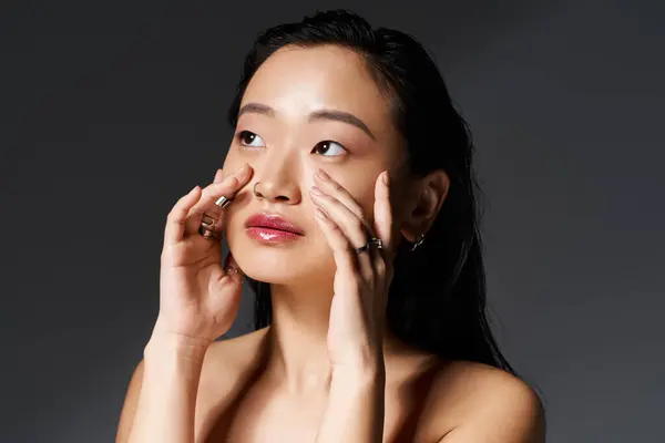 Jeune femme asiatique embrasse un moment tranquille, en appliquant doucement des soins de la peau dans un éclairage doux. — Photo de stock