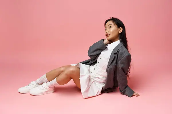 Una giovane donna asiatica posa con grazia sul pavimento in un abito elegante in mezzo a uno sfondo rosa brillante. — Foto stock