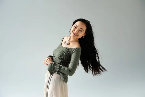 Joyeuse jeune femme asiatique dans une tenue fluide sourit et joue avec ses cheveux dans un studio serein. — Photo de stock