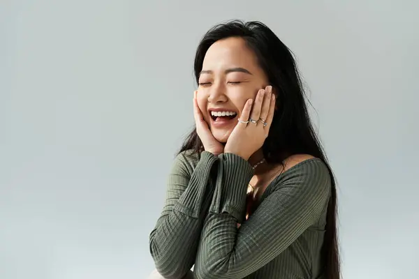 Une jeune femme asiatique sourit, les mains sur les joues, savourant la joie pure. — Photo de stock
