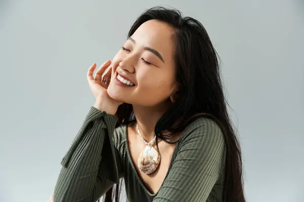 Deliziosa giovane donna asiatica con i capelli lunghi irradia felicità mentre poggia il mento sulla mano. — Foto stock