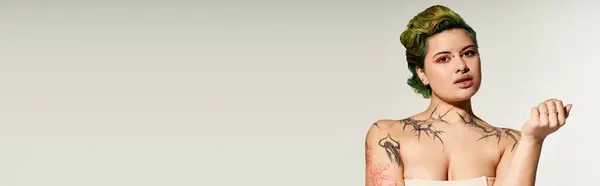 A young woman expresses her vibrant style with artistic tattoos and fashionable makeup in a studio. — Stock Photo