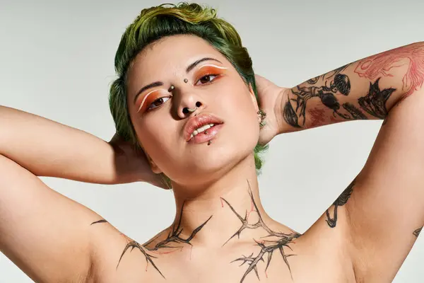 A young woman with vibrant hair displays her stylish makeup and tattoos in an expressive pose. — Stock Photo