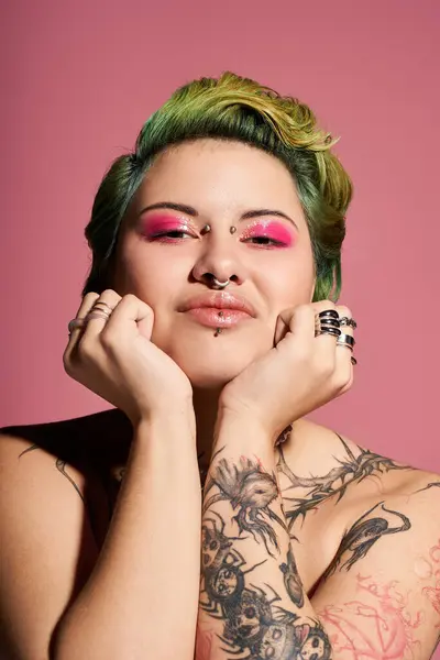 A young woman with green hair exhibits her unique style and artistic makeup on a pink backdrop. — Stock Photo