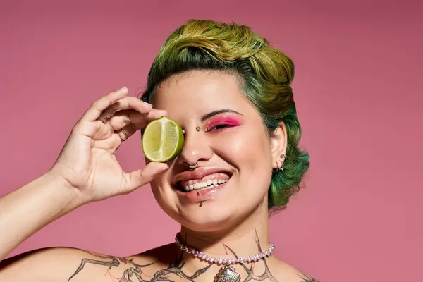 A cheerful young woman holds a lime to her eye, flaunting her stylish makeup and vibrant hair. — Stock Photo