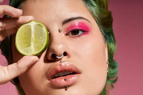 A young woman holds a lime to her eye, highlighting her bold makeup in a vibrant, colorful setting. — Stock Photo