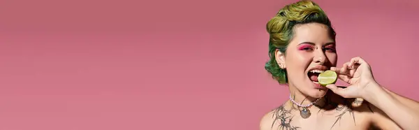 A young woman with vibrant makeup playfully bites a lime against a pink backdrop. — Stock Photo
