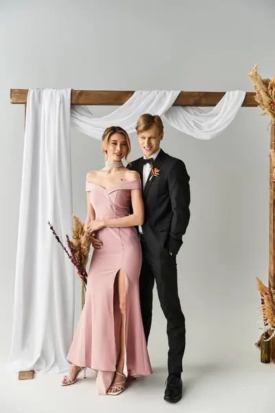Joyful young couple poses together under a decorative arch, celebrating their spring wedding. — Stock Photo