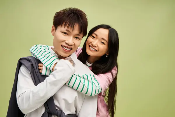 A stylish couple smiles and embraces warmly, dressed in trendy outfits against a green backdrop. — Stock Photo