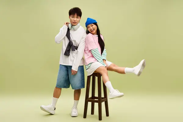 Stylish couple poses playfully, radiating love and energy in matching trendy outfits on a stool. — Stock Photo
