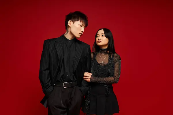 A lovely couple stands closely together, exuding love and fashion against a bold red background. — Stock Photo
