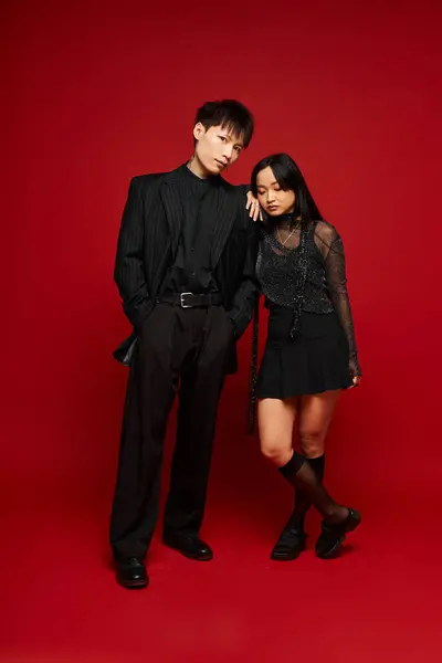 A stylish couple exudes love and elegance in trendy outfits against a vivid red backdrop. — Stock Photo