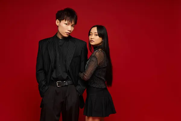 A stylish couple poses closely, displaying their chemistry against a vibrant red backdrop. — Stock Photo