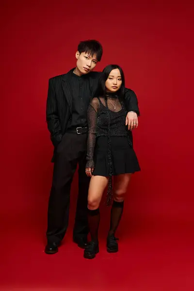 Love blooms as a couple showcases fashionable attire against a vibrant red backdrop. — Stock Photo