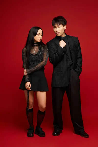 A lovely couple stands together, showcasing their stylish outfits against a vibrant red background. — Stock Photo