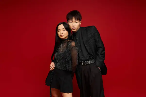 Stylish couple stands close together against a bold red backdrop, exuding love and confidence. — Stock Photo