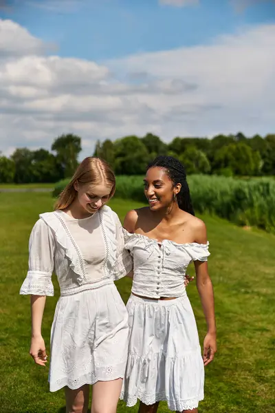 Two young women in white dresses stroll together, savoring the sunshine and company. — Stock Photo