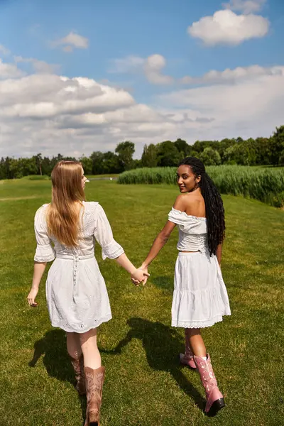 Two women in white dresses walk together in a lush field, celebrating their love. — Stock Photo