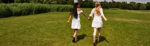 Two women walk hand in hand through a lush field, smiling and sharing a joyful moment. — Stock Photo