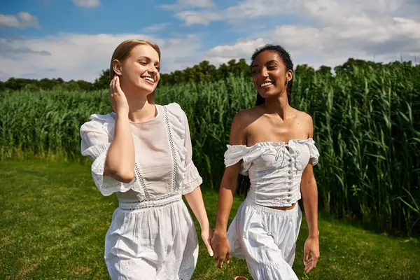 Two beautiful women walk hand in hand, radiating joy against a backdrop of vibrant greenery. — Stock Photo