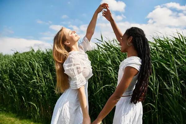 Two young women celebrate their love, dancing happily amid tall grass under a clear blue sky. — Stock Photo