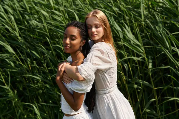 Two beautiful women embrace in sunlit green grass, sharing an intimate moment. — Stock Photo